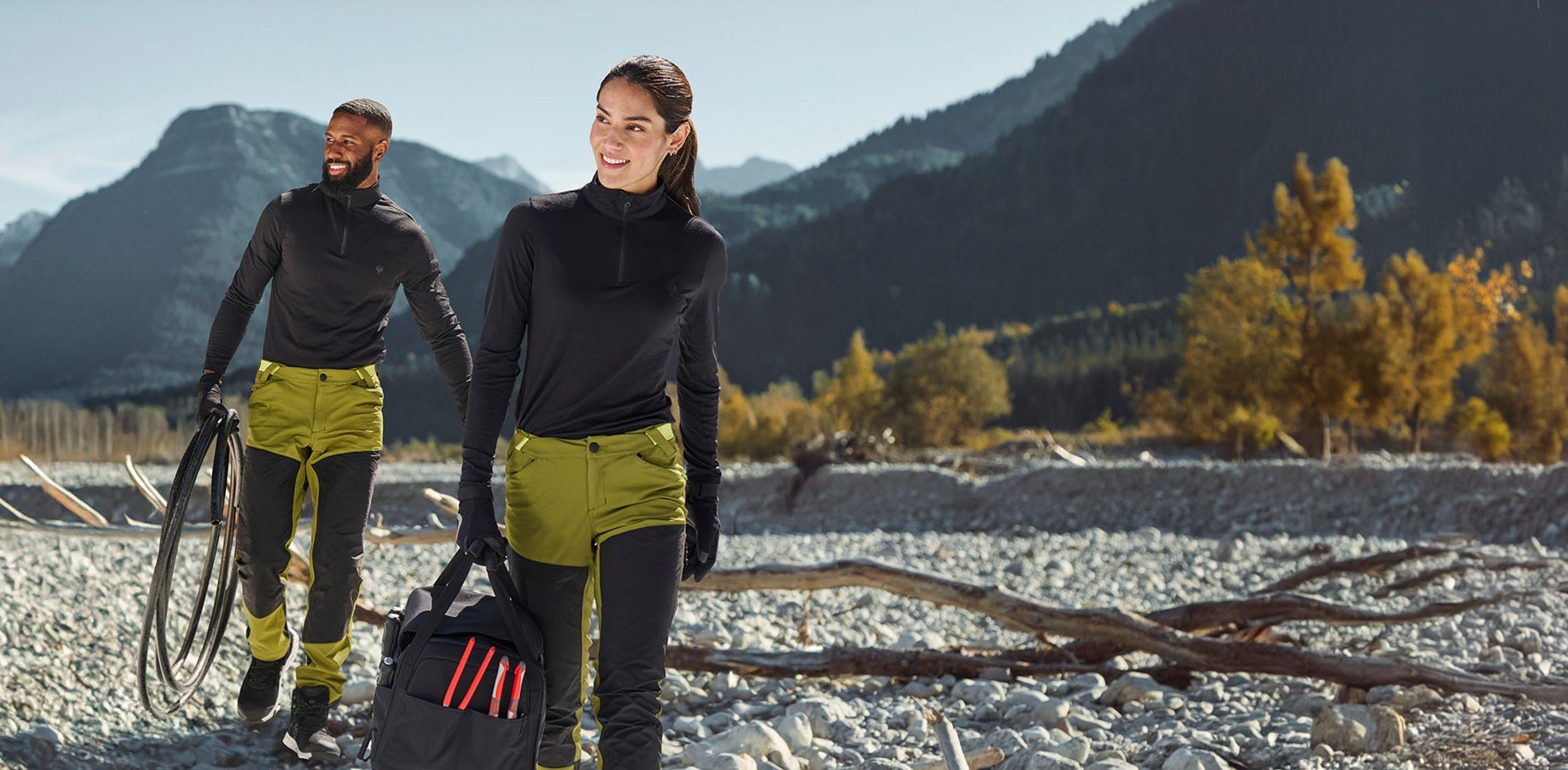 Un uomo e una donna indossano pantaloni funzionali ibridi e.s.trail in verde ginepro/verde lime e troyer in nero
