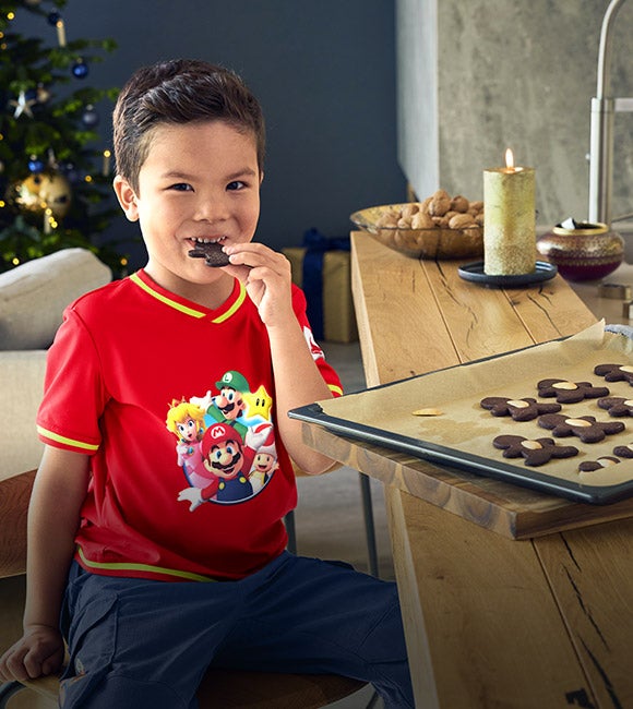 Un ragazzo indossa abbigliamento della collezione Super Mario x Strauss, sedendo su un bancone mangiando biscotti
